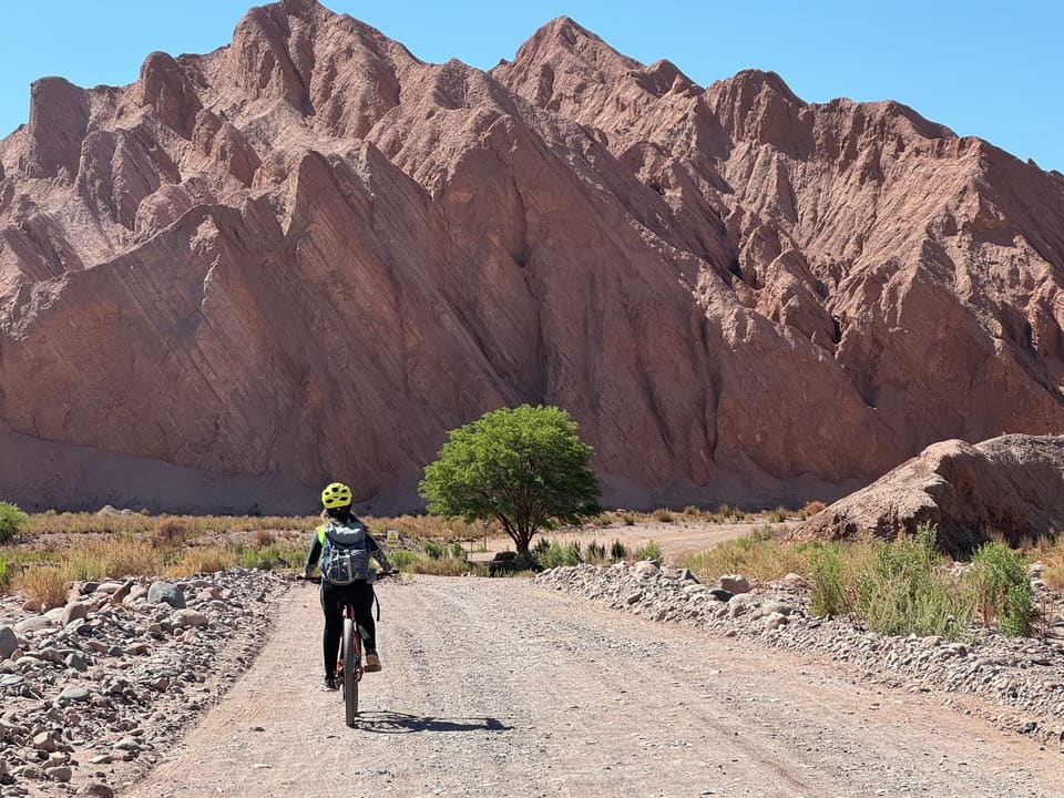Ciclista em estrada de terra com montanhas avermelhadas