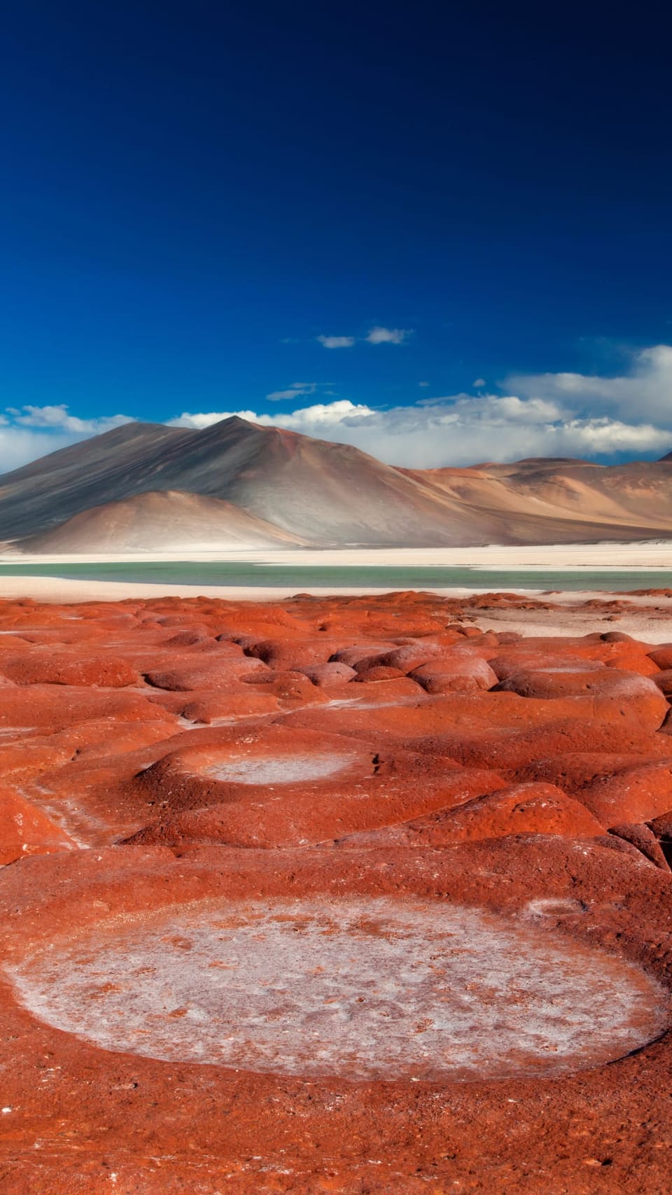 Rochas vermelhas de Piedras Rojas diante de uma lagoa e de montanhas sob céu azul intenso