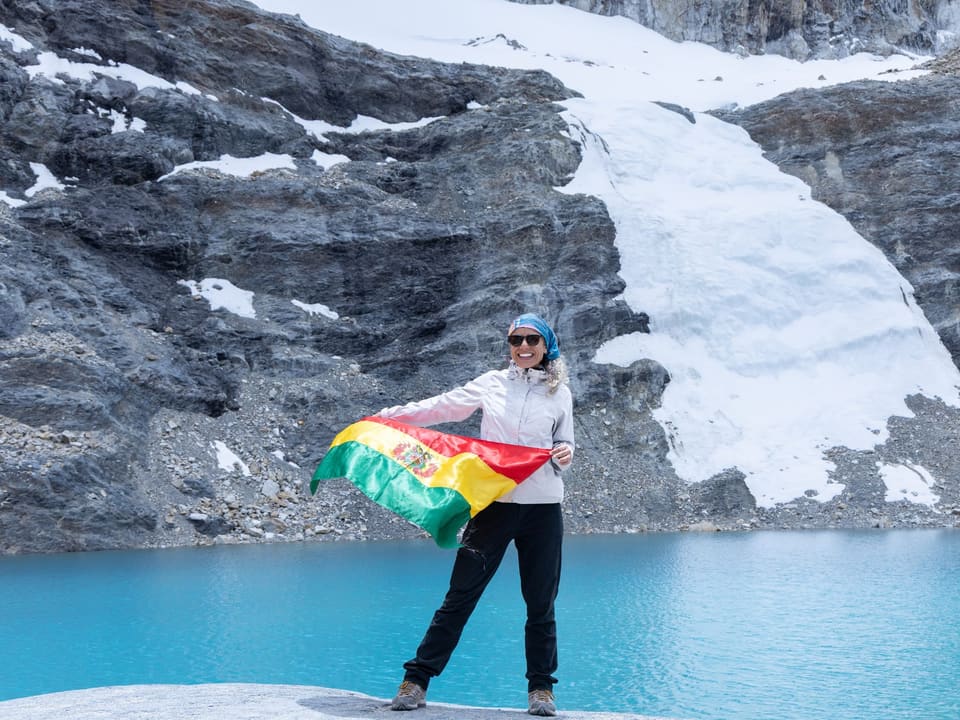 Viajante com a bandeira da Bolívia diante da Laguna Esmeralda e da geleira