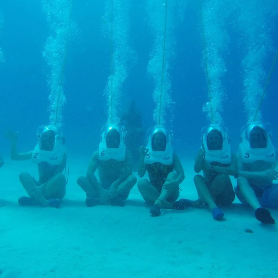 Grupo de aquanautas com capacetes sentado no fundo do mar