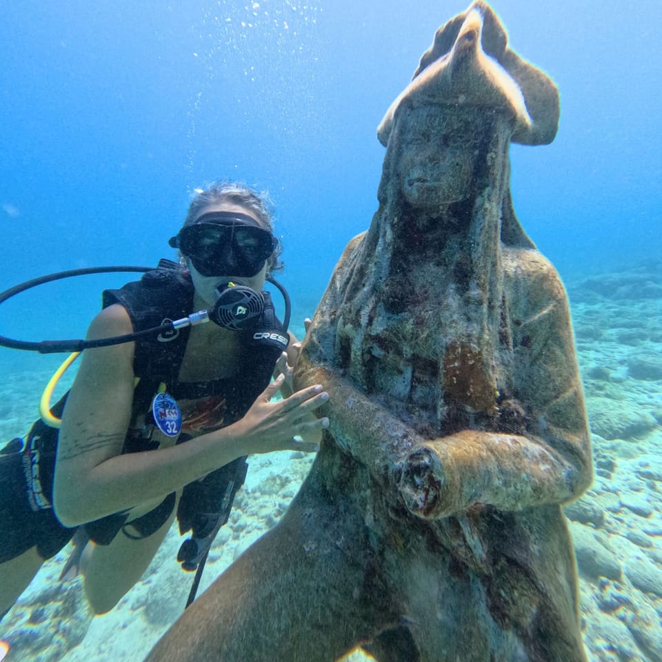 Mergulhadora ao lado de uma estátua submersa
