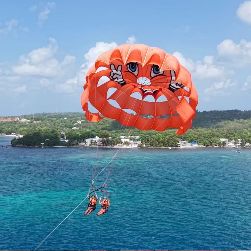 Paraquedas laranja sobre o mar com a ilha ao fundo