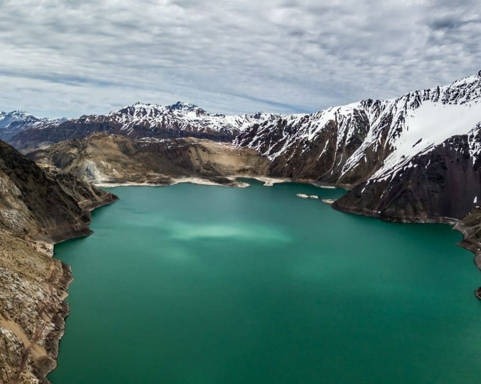 Embalse El Yeso de águas turquesa cercado por montanhas com neve